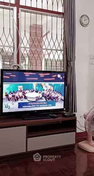 Cozy living room with TV and modern furniture, featuring a large window with security bars.