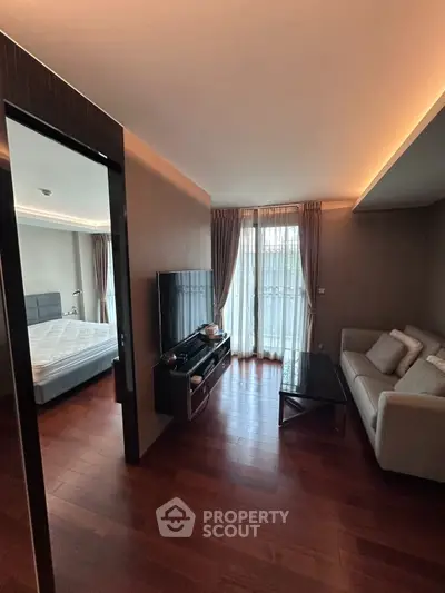 Modern living room with wooden flooring, cozy sofa, and large TV, adjacent to a stylish bedroom with natural light.