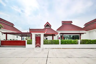 Charming red-roofed house with lush greenery and spacious driveway, perfect for family living.