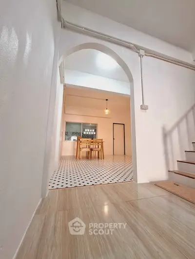Spacious dining area with modern wooden table and chairs, featuring stylish tile flooring and archway entrance.
