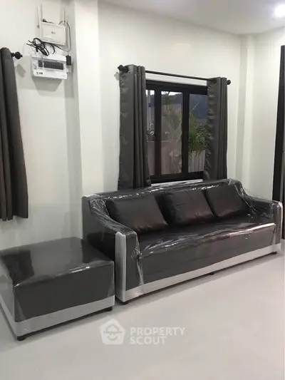 Modern living room with sleek black sofa and large window, perfect for stylish urban living.