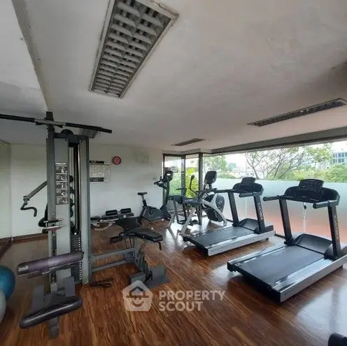 Spacious gym with modern equipment and large windows offering natural light.