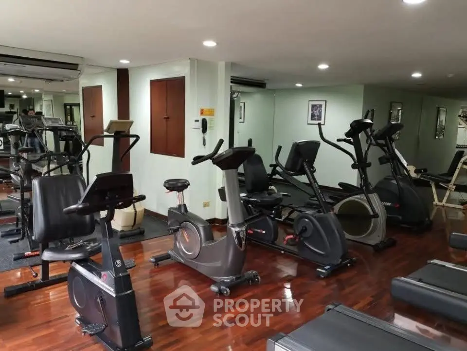 Spacious gym with modern exercise equipment and wooden flooring in a residential building.