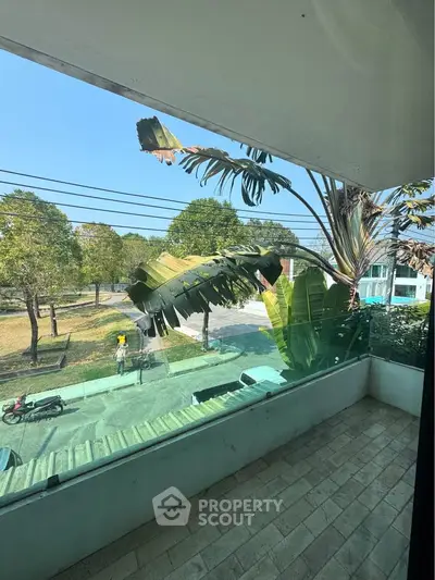 Spacious balcony with glass railing overlooking lush greenery and street view.