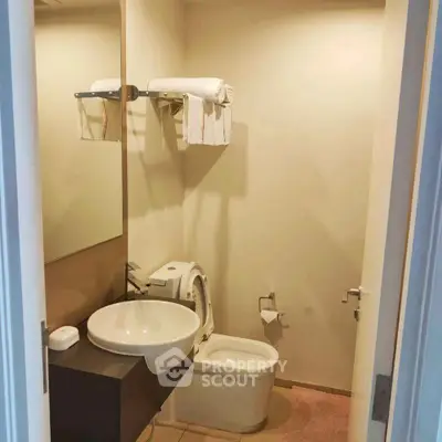 Compact bathroom with modern sink and toilet, featuring a towel rack and mirror.
