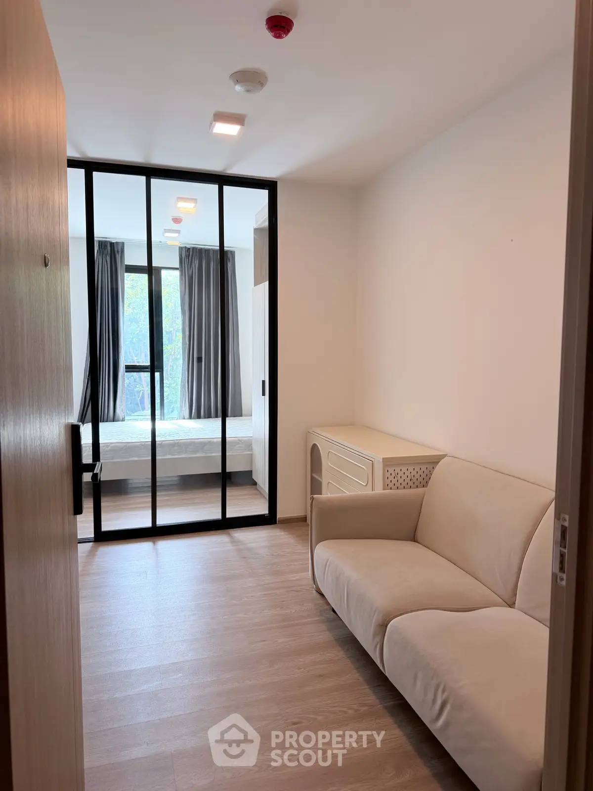 Modern apartment with cozy living area and glass partition leading to bedroom, featuring sleek design and natural light.