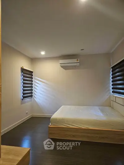Modern bedroom with minimalist design and air conditioning, featuring sleek blinds and wooden flooring.