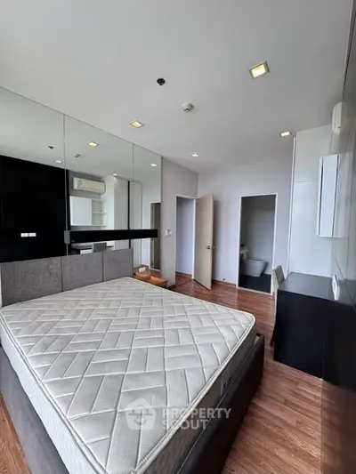 Modern bedroom with large mirror, stylish furniture, and wooden flooring in a contemporary apartment.