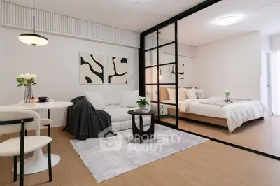 Modern open-plan living room with stylish decor and cozy bedroom separated by glass partition.