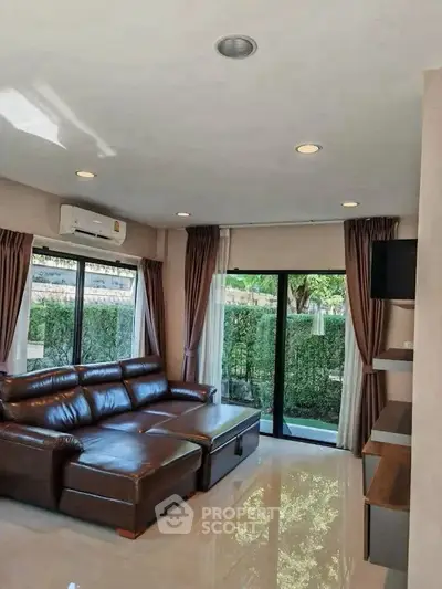 Spacious living room with leather sofa and garden view, perfect for relaxation and entertainment.