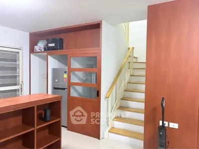 Modern interior with wooden accents, featuring a staircase and kitchen area with a fridge.