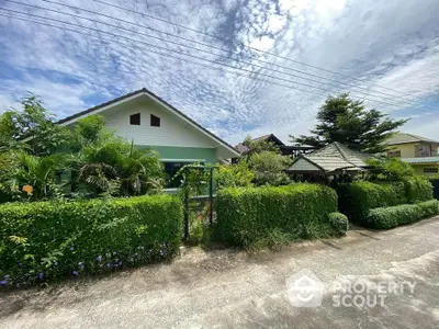 Charming suburban house with lush garden and green hedges under a vibrant sky.