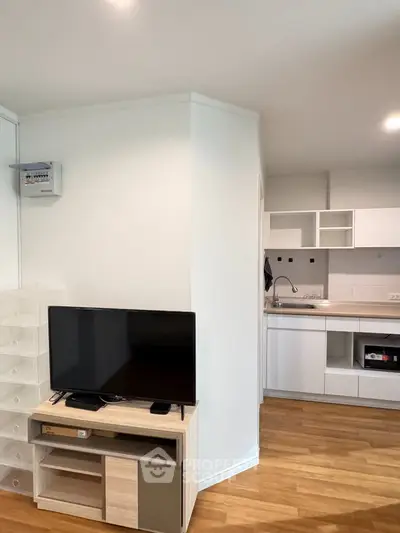 Modern living room with sleek kitchen, wooden flooring, and stylish TV setup.