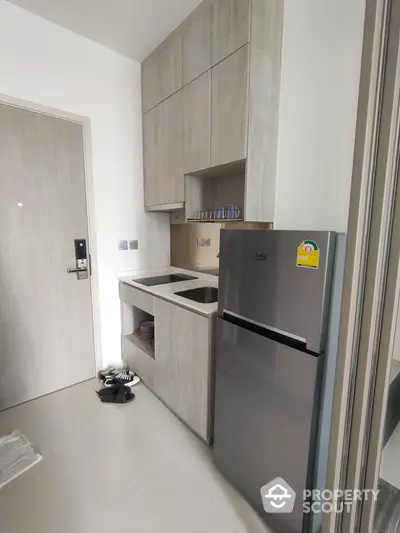 Modern compact kitchen with sleek cabinetry and stainless steel fridge in a stylish apartment.