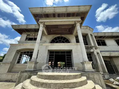 Grand unfinished mansion with classical columns and arched windows under a clear blue sky.