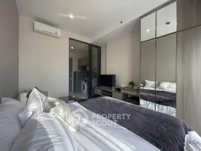 Modern bedroom with mirrored wardrobe and view into kitchen area, featuring sleek design and natural light.