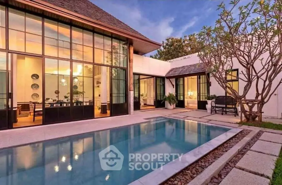 Luxurious modern villa with stunning pool and elegant glass facade at sunset.