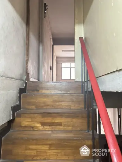 Inviting wooden staircase with contrasting black steps and a vibrant red handrail leading to a bright upper level, enhancing the property's character.