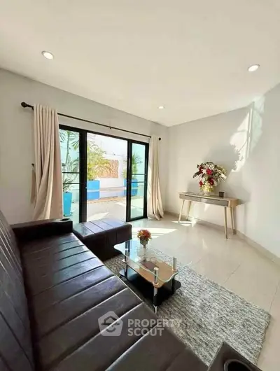 Modern living room with sleek leather sofa and glass coffee table, overlooking a bright outdoor area.