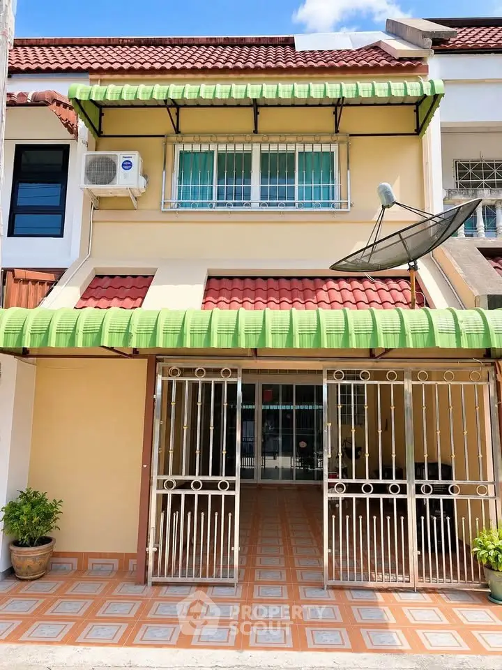 Charming townhouse with tiled patio and green awnings, featuring a satellite dish and air conditioning unit.