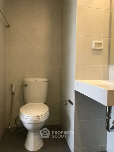 Modern bathroom with sleek design and neutral tiles, featuring a toilet and sink.