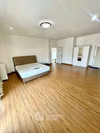 Spacious bedroom with wooden flooring and modern furnishings in a bright apartment.