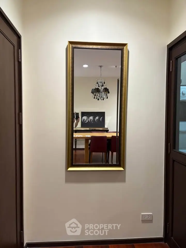 Elegant hallway with a stylish mirror reflecting a dining area and chandelier, enhancing the space's sophistication.