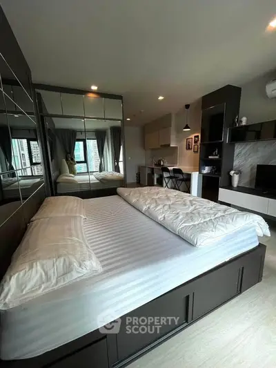 Modern studio apartment with stylish bedroom and open kitchen layout, featuring sleek mirrored wardrobe and cozy ambiance.