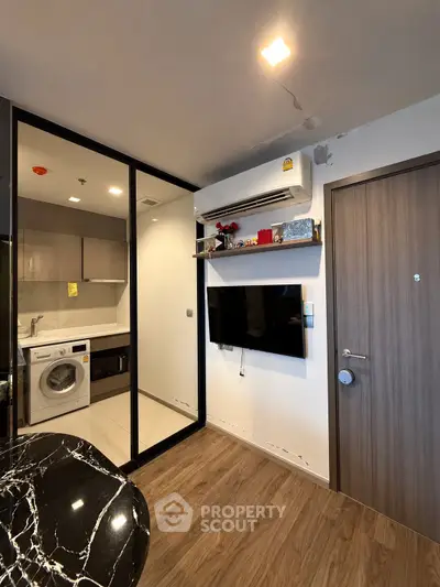 Modern apartment interior with washing machine and wall-mounted TV, featuring sleek design and wood flooring.