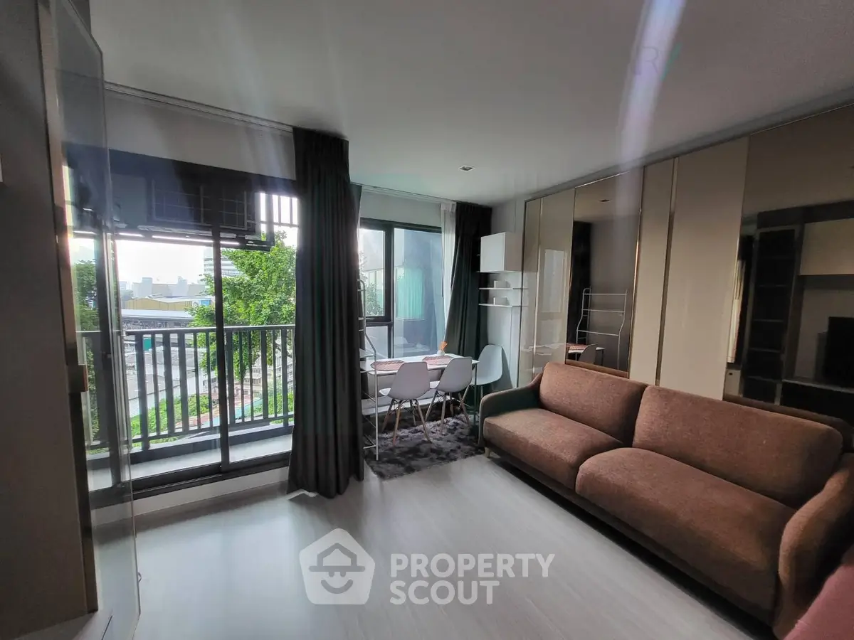 Modern living room with balcony view, stylish furniture, and ample natural light in urban apartment.