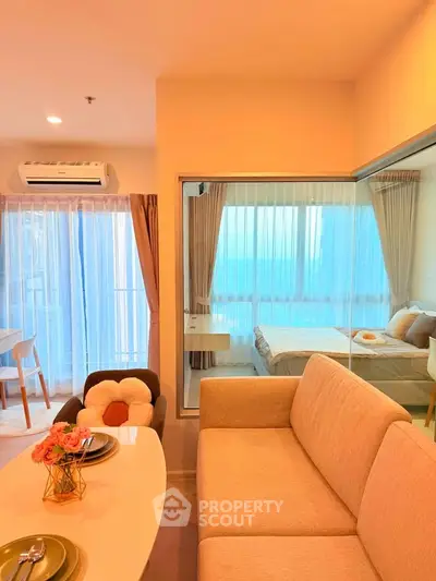 Modern open-plan living room with cozy seating and a view into a stylish bedroom, featuring large windows and elegant decor.