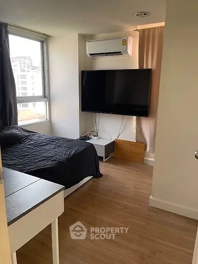 Modern bedroom with large TV and air conditioning, featuring wooden flooring and natural light.