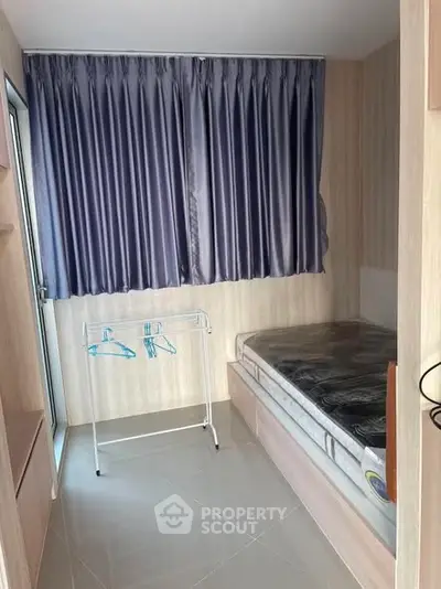 Compact bedroom with bed, curtain, and clothes rack in modern apartment.