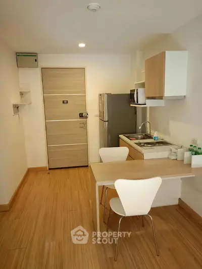 Modern compact kitchen with wooden flooring and sleek appliances in a cozy apartment.