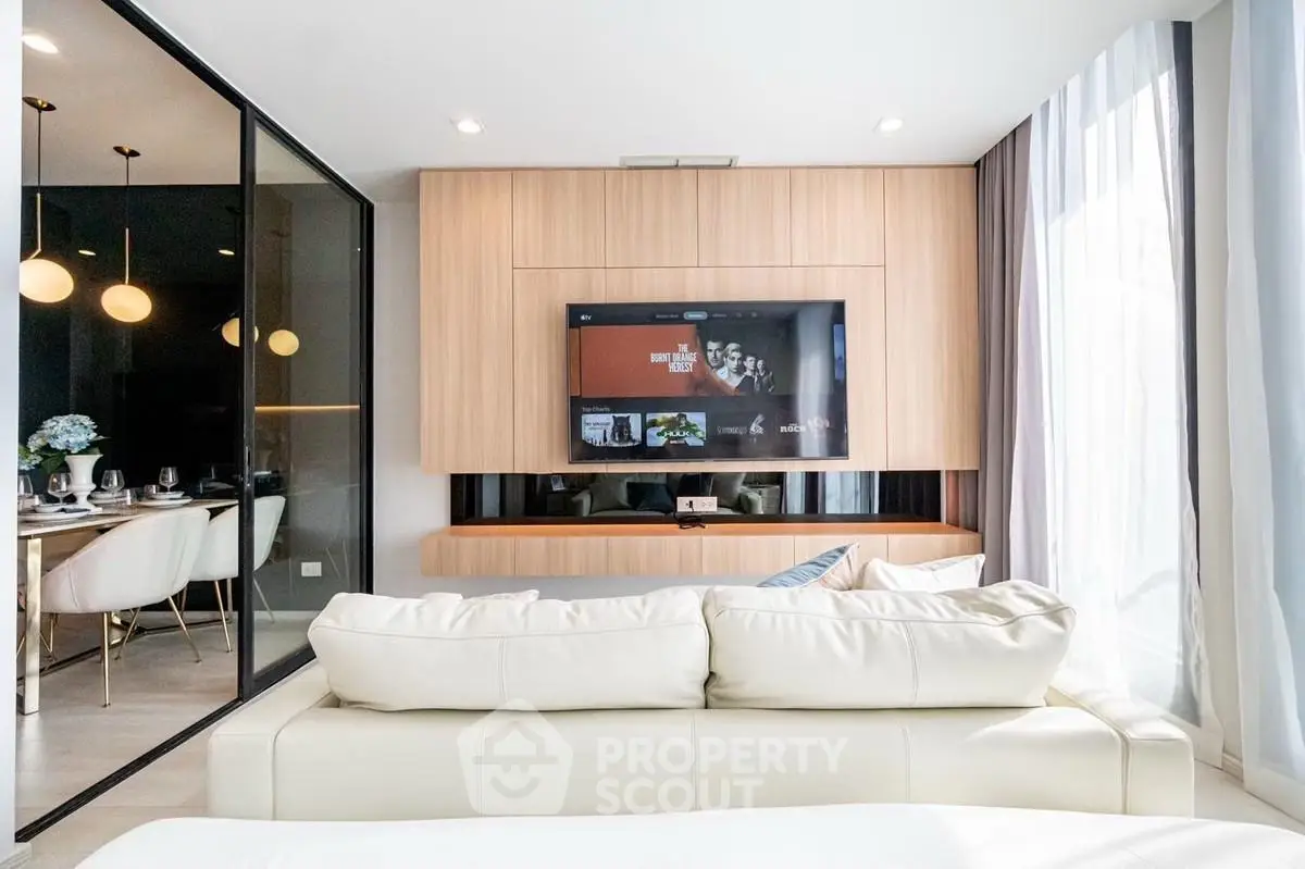 Modern living room with sleek design, featuring a wall-mounted TV and elegant dining area with glass partition.