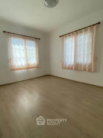 Bright empty room with wooden flooring and sheer curtains, perfect for customization.