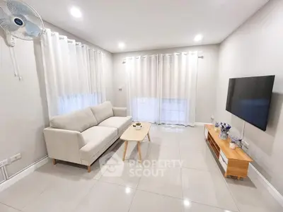 Modern living room with sleek furniture and wall-mounted TV, featuring bright lighting and elegant decor.