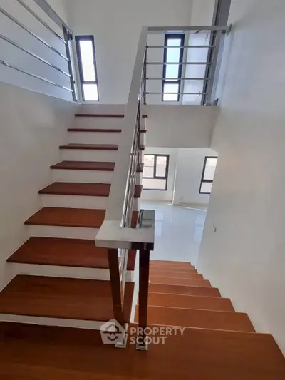 Modern staircase with sleek metal railings and wooden steps in bright interior.