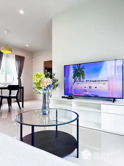 Modern living room with sleek furniture and large TV, open dining area, bright and inviting space.