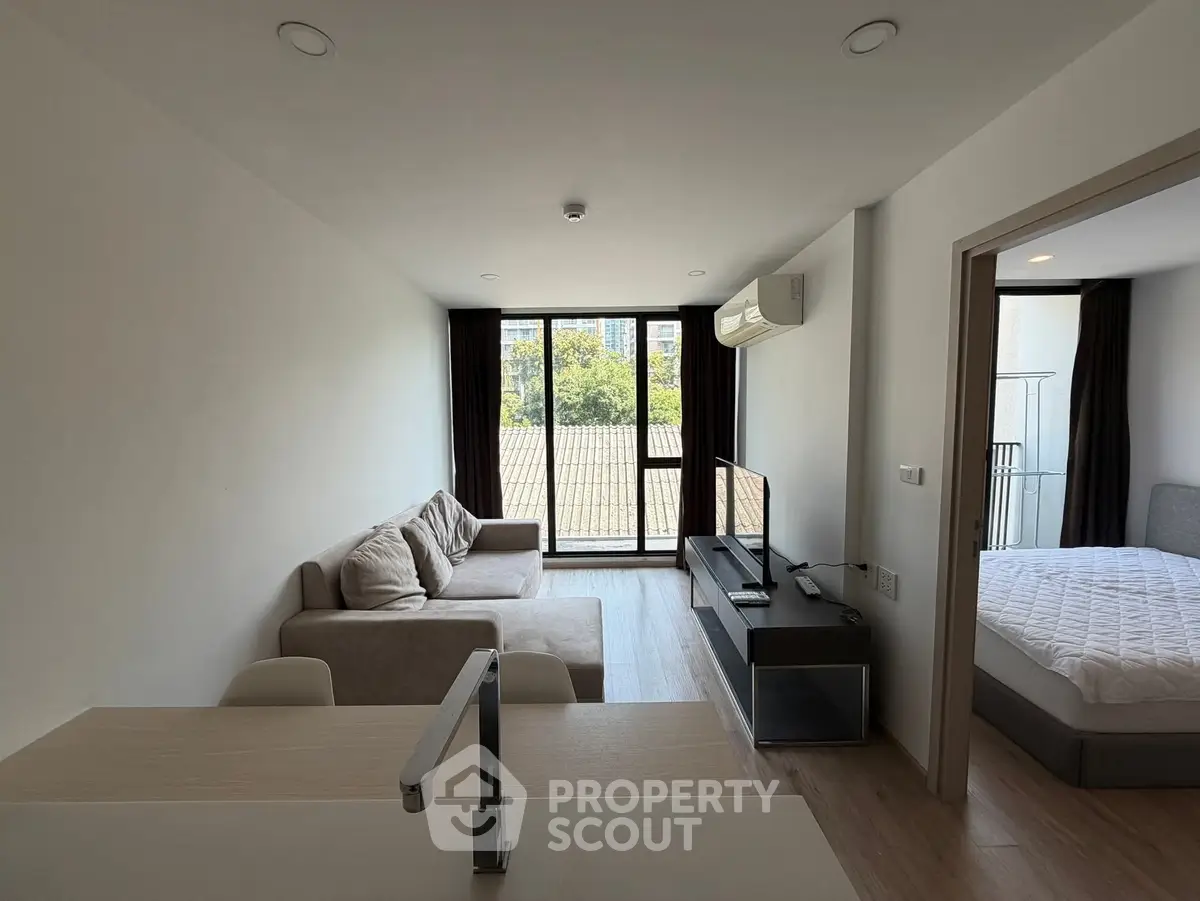Modern living room with balcony view and cozy bedroom in open layout apartment.
