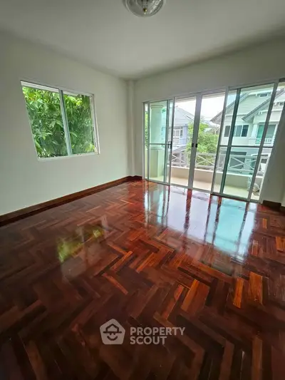 Spacious empty room with polished wooden floors and large windows offering natural light and garden views.