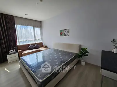 Spacious bedroom with modern decor and natural light, featuring a cozy sofa and stylish artwork.