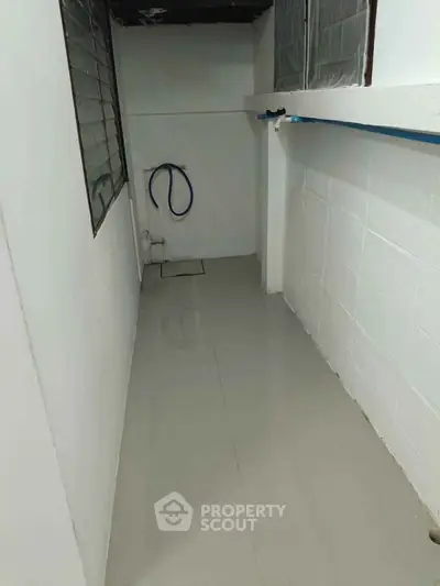 Narrow utility space with tiled floor and plumbing fixtures, ideal for storage or laundry area.