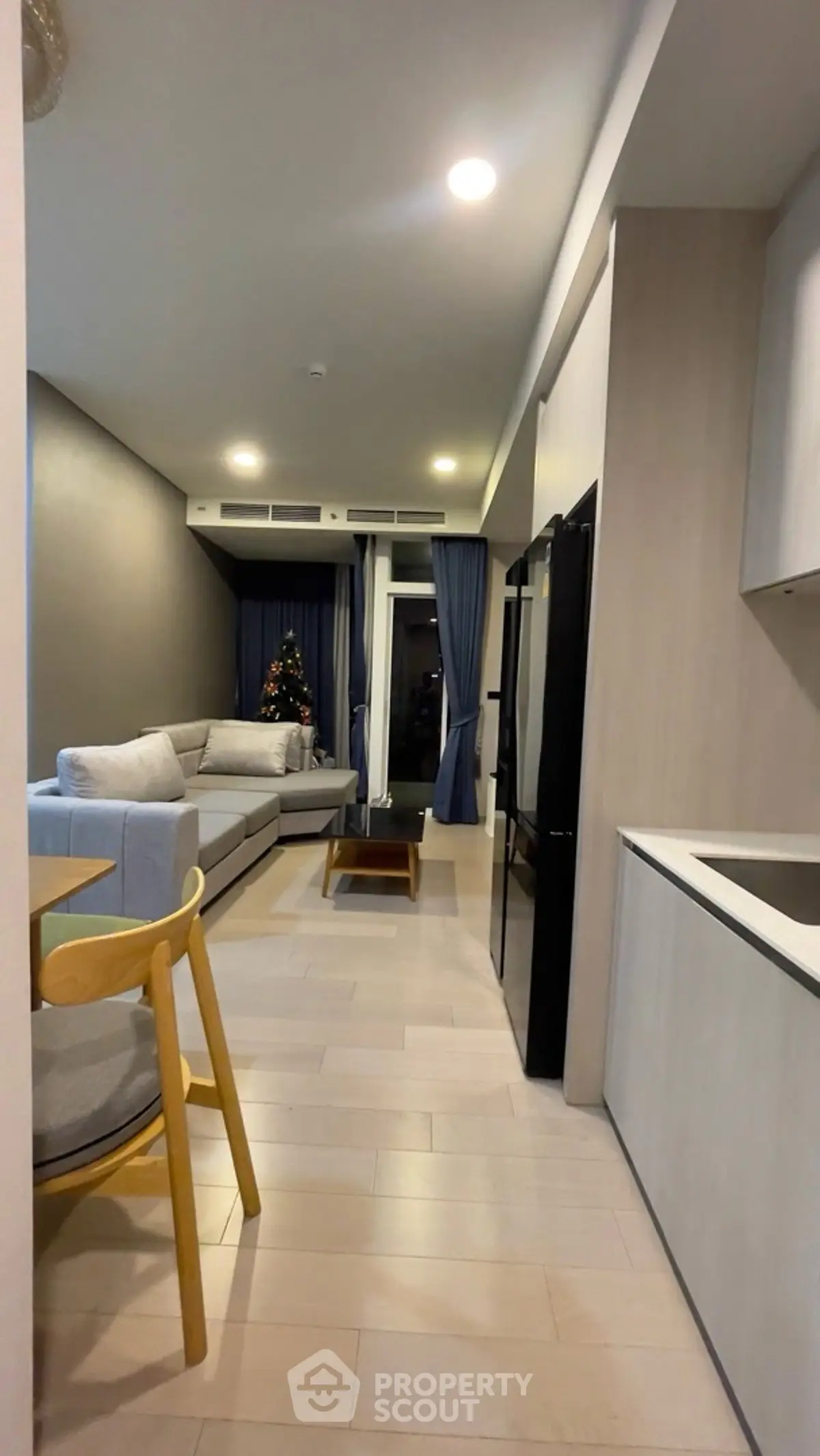 Modern living room with cozy sofa and Christmas tree, open layout with kitchen area.
