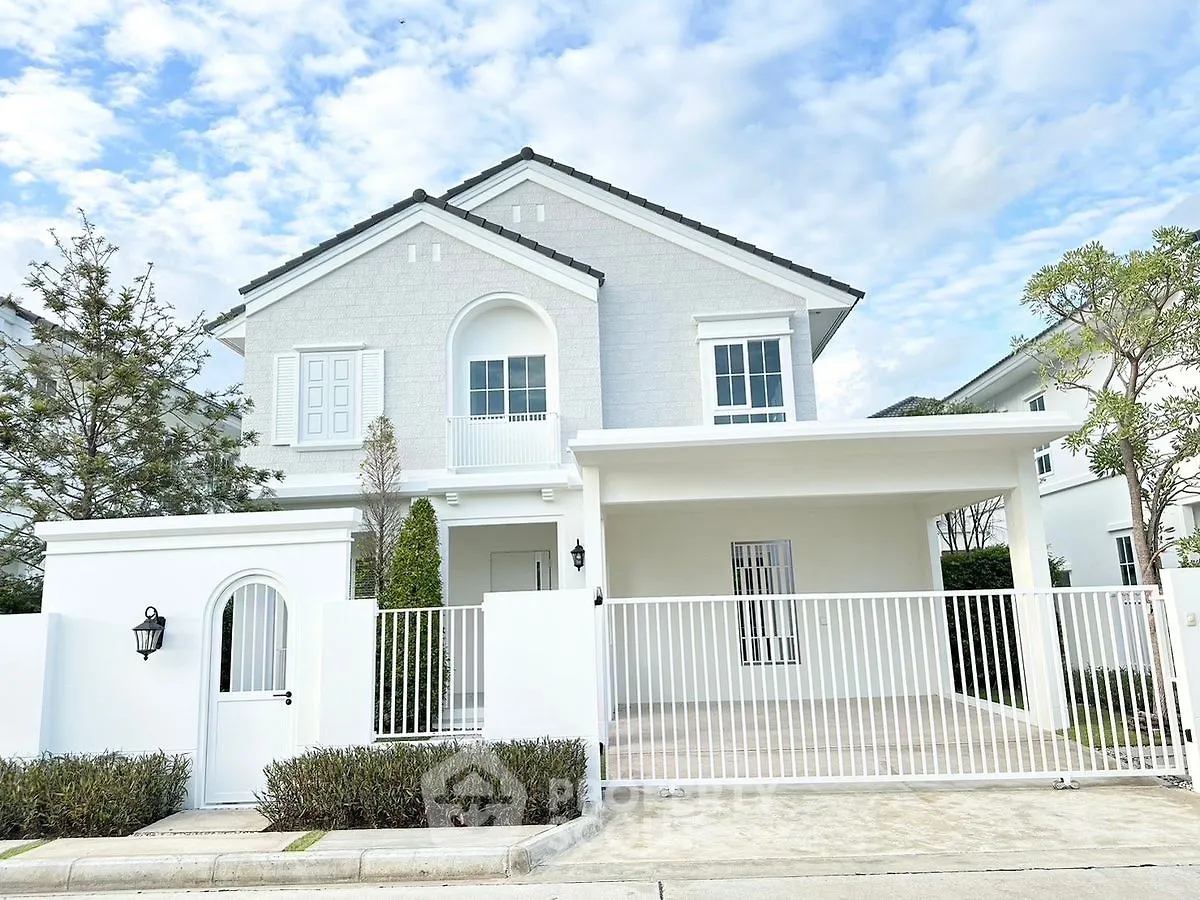 Elegant two-story white house with gated entrance and lush greenery
