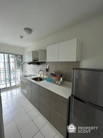 Modern kitchen with stainless steel appliances, ample cabinetry, and sleek countertops, opening to a bright space with balcony access.