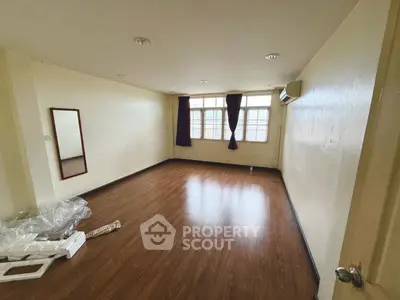 Spacious empty room with wooden flooring and large windows, perfect for customization.