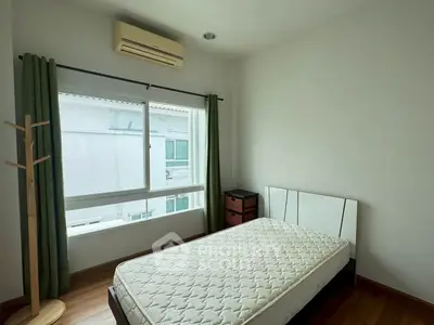 Cozy bedroom with large window and air conditioning, featuring a comfortable mattress and wooden flooring.