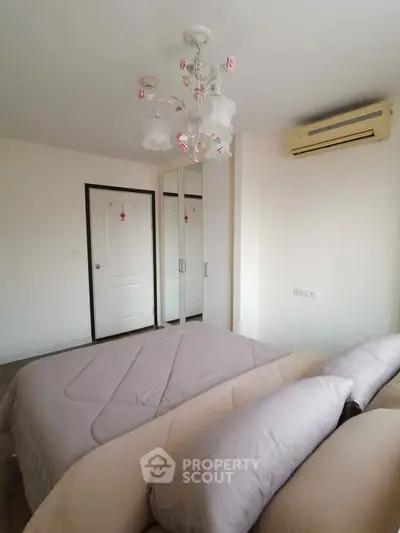 Cozy bedroom with elegant chandelier and mirrored closet doors, featuring soft bedding and air conditioning.