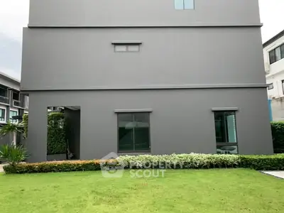 Modern gray building exterior with lush green lawn and shrubs